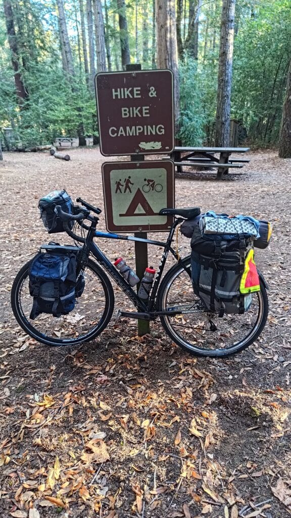 A loaded touring bicycle leaning against a sign reading Hike and Bike Camping
