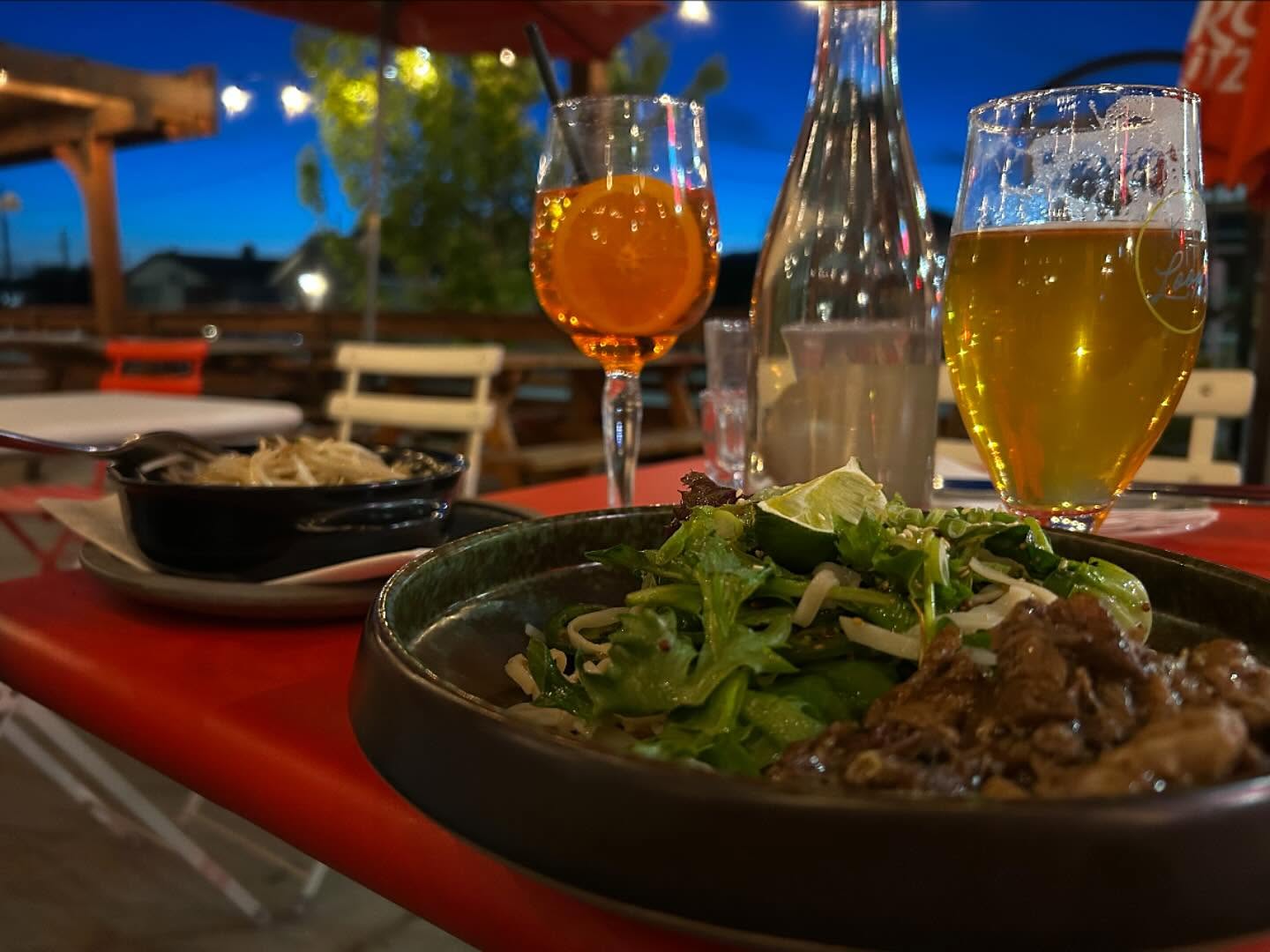 Evening patio at Red Beard Cafe: plates and drinks on a red table under string lights at dusk